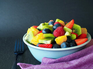 Fruit salad in a bowl on black background (kiwi, orange, strawberry, blueberry)