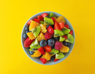 Fruit salad in a bowl on yellow background (kiwi, orange, strawberry, blueberry)
