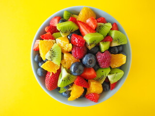 Fruit salad in a bowl on yellow background (kiwi, orange, strawberry, blueberry)
