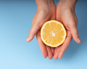 Female hand holding yellow juicy cut lemon on blue background.