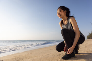 Asian healthy sport woman tying shoelace prepare for running on beach in morning