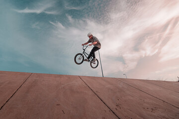 young bmx rider wearing a white helmet jumping on a ramp with the bike