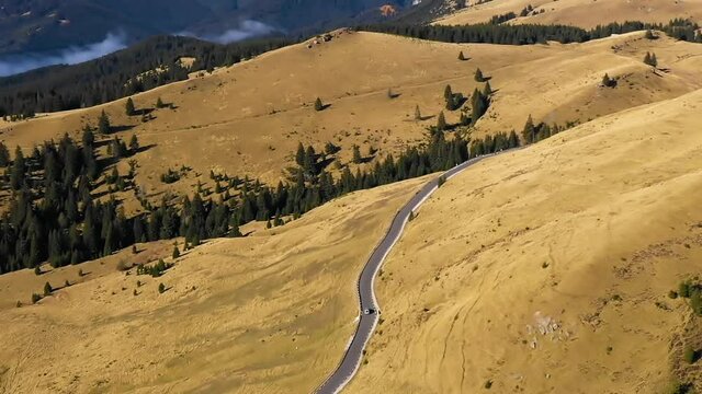 Aerial view of car driving down country road through rural rolling hills and mountain. High altitude road. Highway on the mountain. Mountain forest with fog and countryside asphalt road. Travel by car