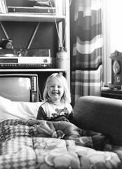 1977 vintage, seventies, retro monochrome image of a young smiling girl with blond hair sitting in a retro sleeping bag.	
