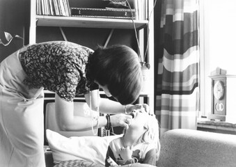1977 vintage, seventies, retro monochrome image of a mother caring for and checking on her sick daughter	

