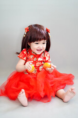 Portrait of an asian cute baby girl in Chinese traditional costume enjoying while holding the sacred oranges in Chinese New Year (Chinese translation : Lucky and happiness)