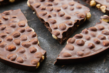 Pieces of milk chocolate with hazelnuts on a dark background, handmade chocolate