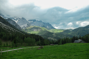 Fototapeta na wymiar A gravelled road through Alpine valley in Austria in the region of Dachstein. High mountain around, partially covered with snow. Stony and sharp mountains. Overcast. Dense forest at the foothill.
