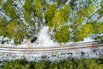 Aerial View Of Black Car On Snow Covered pine forest road in Northern Europe