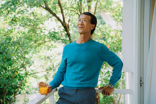 Portrait Of Senior Man In Blue Sweater Holding Orange Juice In A Park.