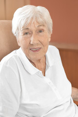 Cheerfully smiling senior woman in a comfy chair in her room at a retirement home.