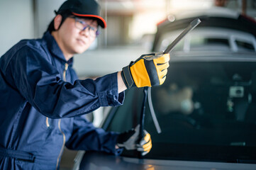 Young Asian auto mechanic checking windshield wiper in auto service garage. Mechanical maintenance...