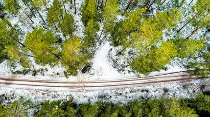 Aerial View Of Black Car On Snow Covered pine forest road in Northern Europe