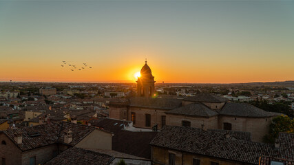 Panorama all'alba di una città vista dall'alto con sole dietro alla cupola di un monumento e...