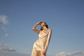 Fashion outdoor portrait of woman in beige silk satin long dress against clear blue sky

