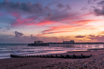 Ribbons of red-lit clouds stretch across the sky above the shore and sea at Worthing, Sussex, UK