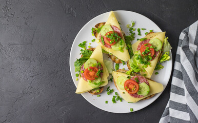 Colorful sandwiches with lettuce cheese and tomato on white plates lying on a dark background top...