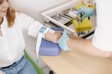 Skillful nurse is doing blood test for woman in clinic. Gilr sitting near table.