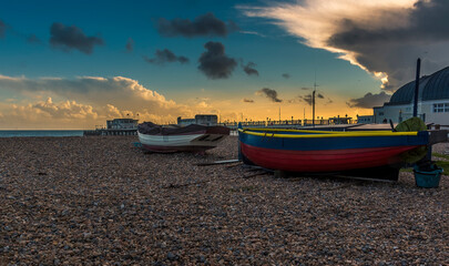 Fototapeta premium A view past boats on the beach at Worthing, Sussex, UK at sunset