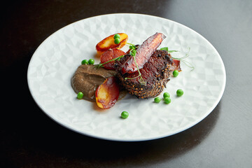 Juicy medium rare beef steak in black pepper with vegetables and mushroom sauce in a white plate on a dark background