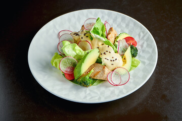 Salad with turkey, avocado and broccoli with cheese sauce in a white plate on a dark background
