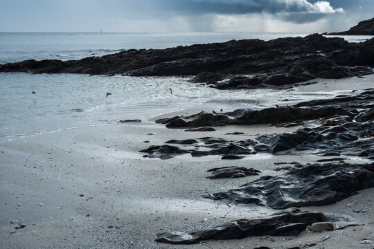 View of a sandy beach and rocky shore under a cloudy sky.