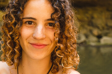 Portrait of a beautiful young caucasian woman captured outdoors in nature. Close up of a curly girl smiling and looking at the camera