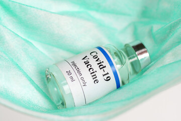 COVID-19 vaccine bottle on green mask background. The vaccination period and the improvement of immunity.