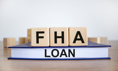FHA loan symbol. Wooden blocks form the words 'FHA loan', book, wooden table. Beautiful white background, copy space. Business and FHA - federal housing administration loan concept.
