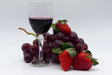 Glass of red wine with bunch of red grapes and strawberries on white background