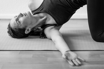 A woman in her early 30's practicing yoga at home on the floor, performing spine twisting asana or...