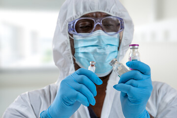 scientist doctor in protection suit working at laboratory holding up new vaccine bottle