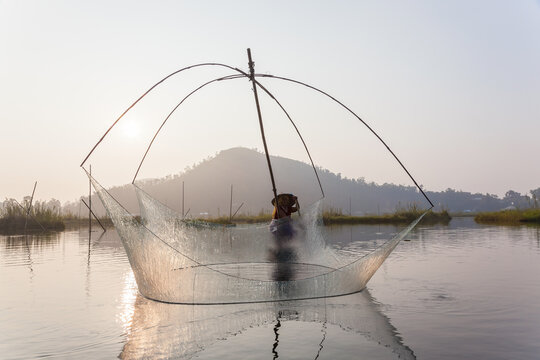 Fisherman on his boat moving arched swing nets above the water at  Loktak Lake