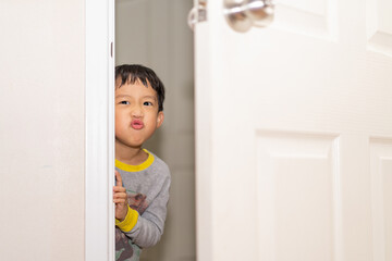 A playful boy peeking from behind the door.