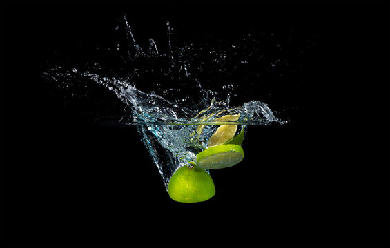 Fresh lime falling into the water isolated on a black background.