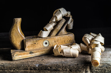 Old wooden planer and wood chips on a wooden plank with dark background.
