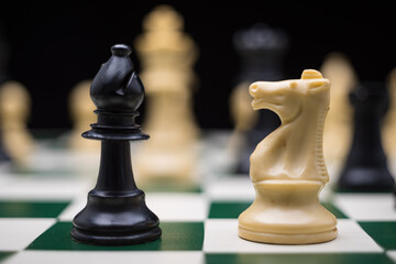 Extreme close up of chess pieces arranged on a portable chessboard before a black background.