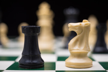 Extreme close up of chess pieces arranged on a portable chessboard before a black background.