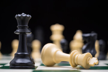 Extreme close up of chess pieces arranged on a portable chessboard before a black background.