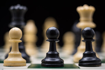 Extreme close up of chess pieces arranged on a portable chessboard before a black background.