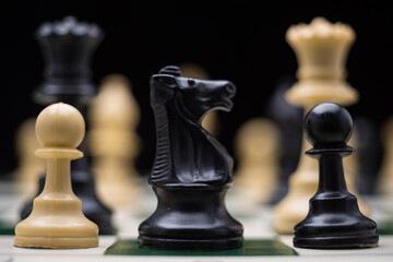 Extreme close up of chess pieces arranged on a portable chessboard before a black background.