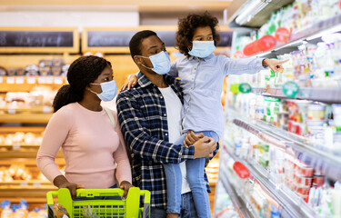 Family shopping during coronavirus pandemic. Black family with child wearing face masks, purchasing...