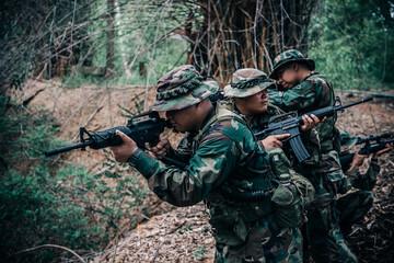 Fototapeta premium Team of army soldier with machine gun moving in the forest,Thai militia soldier in combat uniforms in the wood,Wander the patrol sloping in the rainforest.