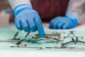 Surgical tools lying on the table while group of surgeons at background operating patient. Steel medical instruments ready to be used.
