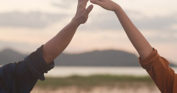 Young asia campers couple standing fist bump at campsite near beach. Happy male and female traveler success and fun when sunset in evening. Outdoor activity, adventure travel, or holiday vacation.