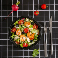 Salad with shrimps, cherry tomato, mixed greens on black geometric background.