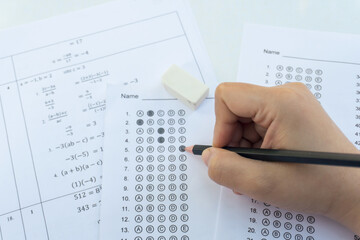 Obraz premium Students hand holding pencil writing selected choice on answer sheets and Mathematics question sheets. students testing doing examination. school exam