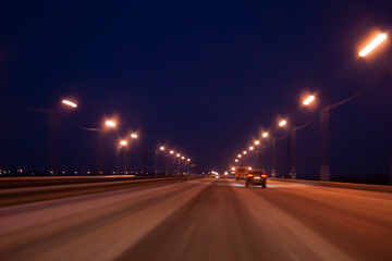 Fototapeta na wymiar Night highway in winter. Light headlights in the dark, the movement of cars from the viewer