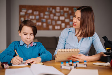 Aunt and nephew do homework together. Women explain kid writes in notebook. Schoolboy studying at...