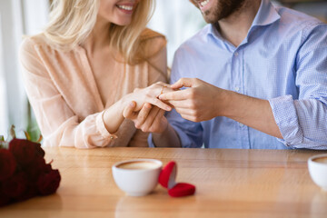 Cropped view of millennial guy holding his fiancee's hand with diamond engagement ring at cafe